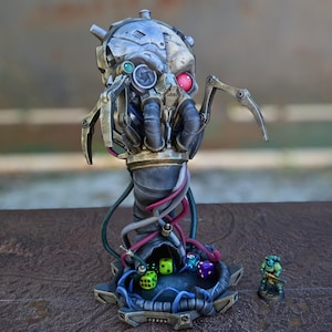 May include: A detailed, metallic sculpture of a robotic skull with mechanical arms and a cylindrical base. The sculpture features a red eye, green and blue lenses, and various wires. Dice are visible in a lower compartment, and a miniature figure stands nearby.