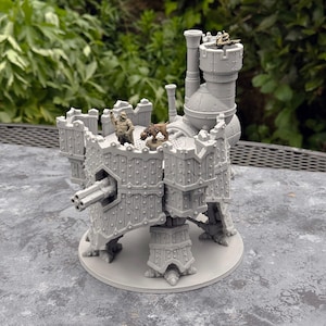 May include: A gray, multi-legged mechanical fortress miniature featuring a central turret, a multi-barreled cannon, and a tall chimney. The structure includes a platform with two small painted figures, one human-like and one animal-like, plus a third figure positioned in the upper tower.
