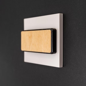 May include: A white square wall plate with a wooden rectangular panel framed in black.
