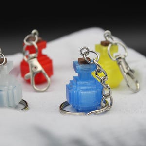 May include: Four small, colourful, 3D printed bottles with keychains. The bottles are blue, white, yellow, and red.