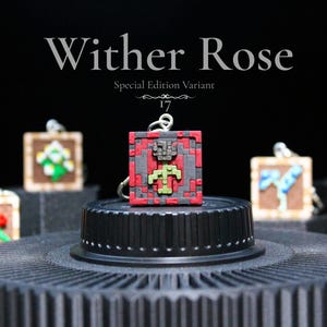 K&ouml;nnte beinhalten: Eine Sammlung pixeliger Anh&auml;nger, jeder mit einem anderen Blumendesign. Der zentrale Anh&auml;nger, mit der Aufschrift "Wither Rose", ist rot, grau und gr&uuml;n. Weitere Anh&auml;nger sind eine Sonnenblume, Rosen und andere Blumen.