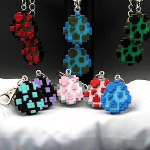 May include: Seven different patterned keychains with silver chains. The keychains are shaped like eggs and feature various color combinations, including red, black, green, blue, pink, and white.