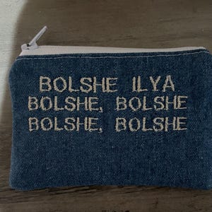 Pu&ograve; includere: Un astuccio con cerniera blu denim con cuciture bianche e una cerniera bianca. L'astuccio presenta un testo ricamato in un colore di filo pi&ugrave; chiaro che recita "Bolshe Ilya Bolshe, Bolshe Bolshe Bolshe, Bolshe".