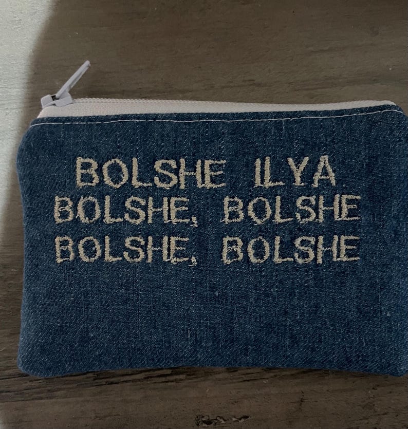 Pu&ograve; includere: Un astuccio con cerniera blu denim con cuciture bianche e una cerniera bianca. L'astuccio presenta un testo ricamato in un colore di filo pi&ugrave; chiaro che recita "Bolshe Ilya Bolshe, Bolshe Bolshe Bolshe, Bolshe".