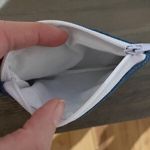 Pu&ograve; includere: Astuccio con cerniera blu denim aperto, con fodera interna bianca. La cerniera bianca &egrave; aperta, rivelando l'interno. Per riporre piccoli oggetti.