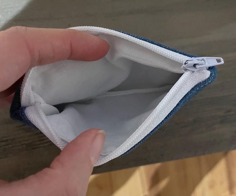 Pu&ograve; includere: Astuccio con cerniera blu denim aperto, con fodera interna bianca. La cerniera bianca &egrave; aperta, rivelando l'interno. Per riporre piccoli oggetti.