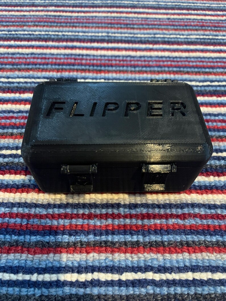 Puede incluir: Una caja de pl&aacute;stico negra con la palabra "FLIPPER" impresa en la parte superior.