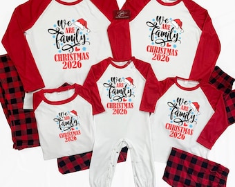 Può includere: Un set di pigiami coordinati per la famiglia con maglie bianche a maniche raglan rosse e pantaloni a quadri rossi e neri. Le maglie riportano la scritta "WE ARE FAMILY CHRISTMAS 2026" in nero e rosso, decorata con un cappellino di Babbo Natale.