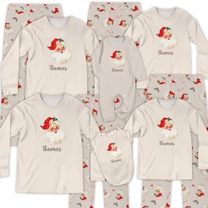 May include: A collection of matching Christmas pajamas in various sizes. The tops are cream-colored with a Santa Claus graphic and the name "Thomas" printed below. The pajama pants are light gray with a repeating pattern of Santa faces and candy canes.