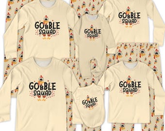 May include: A collection of matching family pajamas in cream, featuring the text "GOBBLE SQUAD" with a cartoon turkey design. The set includes long-sleeved shirts, pants, a onesie, and a dog shirt, all with a Thanksgiving theme.