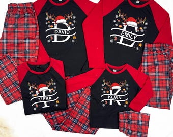 May include: Matching family Christmas pajamas. Black shirts with red sleeves and plaid pants. Each shirt features a reindeer design with a Santa hat and a personalized name: David, Emily, Tiera, and Kevin. The pants are red and blue plaid.