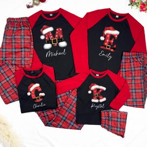 May include: Matching family Christmas pajamas. Black shirts with red sleeves and plaid pants. Each shirt features a letter in a Santa Claus design with a name below: Michael, Emily, Charlie, and Krystal.