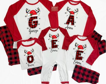 Op de afbeelding: Bijpassende kerstpyjama's voor het gezin in wit en rood. De shirts hebben rode mouwen en een rendierontwerp met een letter en naam. De pyjamabroeken zijn rood en zwart geruit. Inclusief een onesie.
