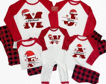 Op de afbeelding: Bijpassende kerstpyjama's voor het gezin in rood, wit en zwart buffelruit. De shirts hebben rode mouwen en witte lijven met een letter- en naamontwerp. De pyjama's bevatten een onesie en een broek.