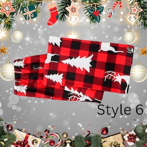 May include: Red and black plaid pajama pants with white Christmas tree and reindeer designs. The pants are folded and displayed on a festive background with holiday decorations. The text "Style 6" is visible.