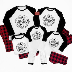 Puede incluir: Conjuntos de pijama a juego para la familia en blanco, negro y cuadros rojos. Las camisas tienen cuerpos blancos y mangas negras, con un gráfico circular que dice "Cousin Crew". Los conjuntos incluyen camisas de manga larga, camisas de manga corta, un body y pantalones a cuadros.