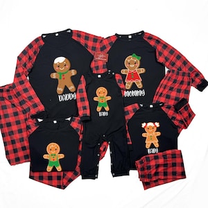 Puede incluir: Pijamas navideños familiares a juego en negro con mangas y pantalones de cuadros rojos. Cada camiseta presenta un gráfico de hombre de jengibre con las palabras "Daddy", "Mommy" y "Baby". El mono del bebé tiene un gráfico de hombre de jengibre.