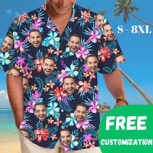 May include: A short-sleeve button-down shirt with a dark blue background featuring a repeating pattern of tropical hibiscus flowers in pink, red, and light blue, interspersed with green palm leaves and a repeating portrait of a smiling man.