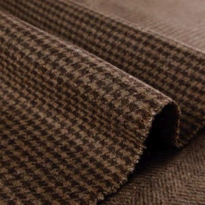 May include: Close-up of a folded brown and tan houndstooth fabric. The fabric has a textured surface and a classic pattern. The material appears to be a medium-weight woven textile, suitable for apparel or home decor projects.