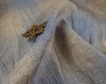 May include: Close-up of blue and grey fabric with a woven star decoration. The fabric has a textured appearance with subtle colour variations. The star is made of woven twigs, adding a natural element to the composition.