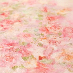 Op de afbeelding: Close-up van een stof met een bloemenpatroon. Het ontwerp toont roze rozen en groene bladeren op een lichtroze achtergrond. De rozen vari&euml;ren in grootte en zijn dicht opeengepakt, wat een romantische en delicate esthetiek cre&euml;ert.