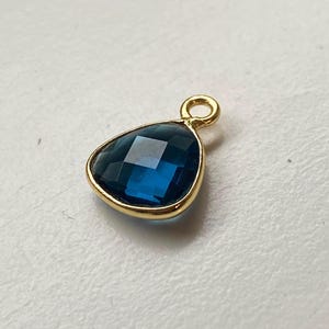 Op de afbeelding: Een gouden hanger met een donkerblauwe edelsteen in een traanvorm.