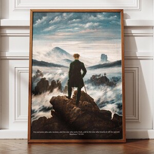 Peut inclure: Une peinture représentant un homme debout sur un sommet de montagne surplombant une mer de nuages. L'homme porte un manteau et un chapeau sombres, et il tient une canne. Le ciel est bleu clair et les nuages sont blancs. La peinture est encadrée dans un cadre en bois.