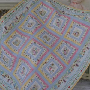 May include: A patchwork quilt featuring a repeating pattern of Peter Rabbit illustrations in square blocks. The quilt is bordered by a floral and character print, with alternating yellow and pink fabric frames surrounding each central rabbit image.