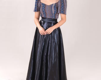 Può includere: Una donna indossa una blusa con maniche a sbuffo a motivi blu e bianchi e una gonna di raso nero. La gonna è lunga e fluida, e la blusa è aderente. La donna è in piedi davanti a uno sfondo bianco. Ternó PH