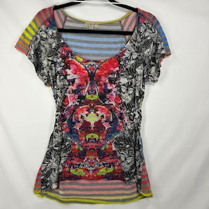 May include: A short-sleeve scoop neck t-shirt featuring a central vibrant red and pink butterfly graphic, surrounded by black and white butterfly patterns. The garment includes horizontal blue, gray, and yellow stripes on the sleeves and hem.