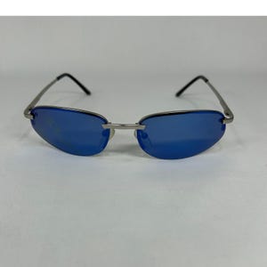 May include: Rimless sunglasses featuring oval-shaped blue lenses and a thin silver-tone metal frame. The eyewear includes a slender bridge connecting the lenses and thin metal temples with black plastic tips at the ends for a secure fit.