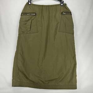 Peut inclure: Une jupe midi vert olive dotée d'une taille élastique, de deux poches avant avec fermetures éclair horizontales et d'un ourlet renforcé par des surpiqûres. La jupe est confectionnée dans un tissu léger et lisse avec un léger éclat.
