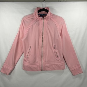 May include: A light pink zip-up jacket featuring a high collar, long sleeves, and two slanted front pockets with silver-toned metal zippers. The garment includes a full-length central silver zipper closure and horizontal stitched detailing at the hem.