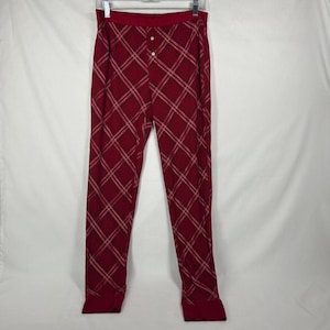 May include: Deep red lounge pants featuring a diagonal plaid pattern in white and light pink lines. The pants have a wide elastic waistband, a front placket with two small white buttons, and fitted cuffs at the bottom of each leg.