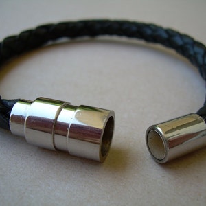 May include: A black leather bracelet with a magnetic clasp. The bracelet is braided and has a silver-toned metal clasp.