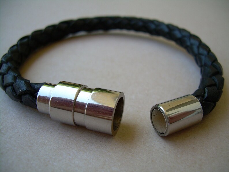 May include: A black leather bracelet with a magnetic clasp. The bracelet is braided and has a silver-toned metal clasp.