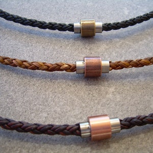Peut inclure: Trois colliers en cuir tress&eacute; avec des accents de perles m&eacute;talliques. Les colliers sont en noir, marron et marron fonc&eacute;.