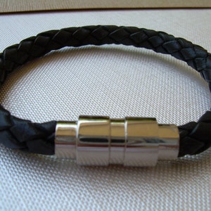 May include: A black leather bracelet with a braided design and a silver magnetic clasp.