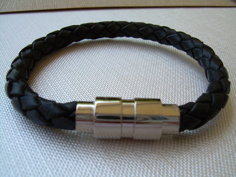 May include: A black leather bracelet with a braided design and a silver magnetic clasp.