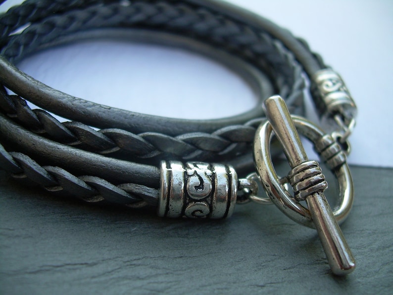 May include: A braided leather bracelet with a silver toggle clasp and decorative bead. The bracelet is made of three strands of leather that are braided together.