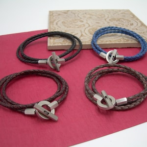 May include: Four leather bracelets with silver metal clasps. Two bracelets are brown, one is black, and one is blue.