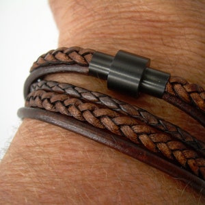 May include: A multi-layered leather bracelet with a braided design and a black metal clasp.