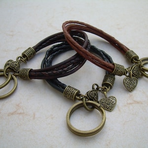 May include: Three leather bracelets with heart charms and key rings. The bracelets are brown, black, and brown. The charms are antique gold.