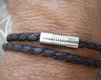 Puede incluir: Un brazalete de cuero marrón con un diseño trenzado y un cierre de metal plateado.