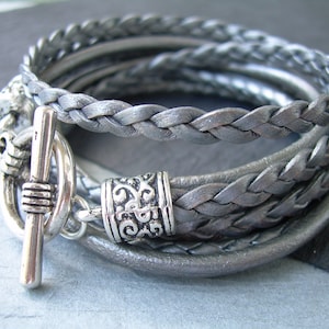 May include: A silver braided leather bracelet with a silver toggle clasp and a decorative silver charm.