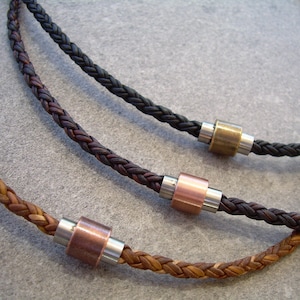Peut inclure: Trois colliers en cuir tress&eacute; avec des perles m&eacute;talliques. Les colliers sont marron, noir et marron clair. Les perles sont argent&eacute;es, cuivr&eacute;es et en laiton.