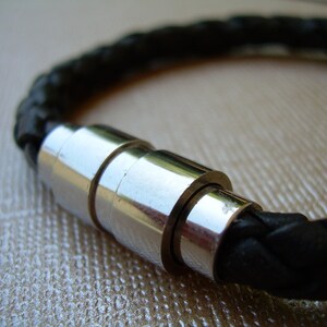 May include: A black leather bracelet with a silver magnetic clasp. The bracelet is braided and has a polished metal finish.