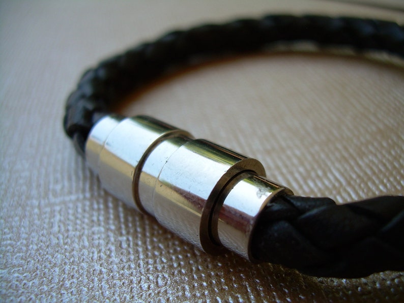 May include: A black leather bracelet with a silver magnetic clasp. The bracelet is braided and has a polished metal finish.