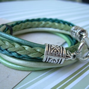 May include: A multi-strand leather bracelet with a braided design in shades of green. The bracelet has a silver clasp and a decorative silver bead.