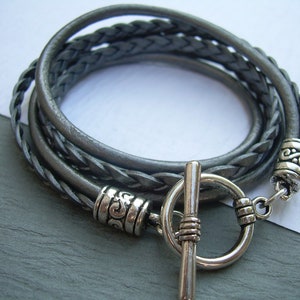 May include: A gray braided leather bracelet with a silver toggle clasp and decorative silver beads.